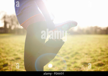 Vista ritagliata della femmina matura runner allungamento della gamba in campo Foto Stock