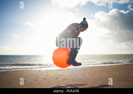 Uomo maturo jumping metà aria sulla tramoggia gonfiabile in spiaggia Foto Stock