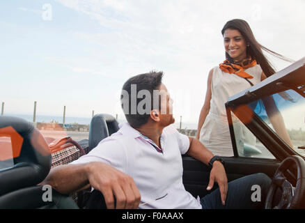 Uomo in autovettura convertibile, donna in piedi accanto a AUTO, sorridente Foto Stock