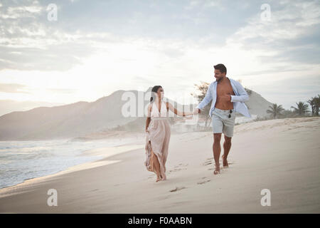 Metà adulto giovane camminando lungo la spiaggia, mano nella mano Foto Stock