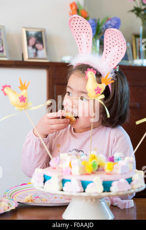 Ragazza giovane indossando orecchie di coniglietto, mangiare la torta Foto Stock