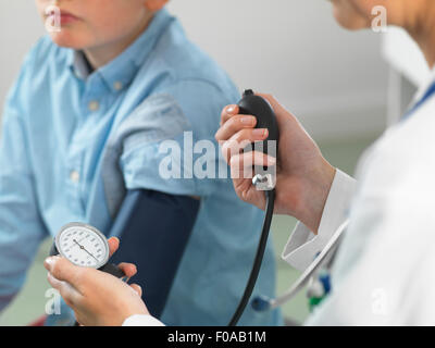 Medico di lettura della pressione sanguigna del giovane ragazzo in clinica Foto Stock