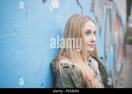 Giovane donna appoggiata contro il muro di graffiti Foto Stock