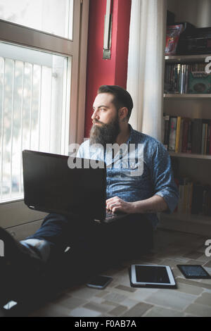 Giovane uomo barbuto utilizzando laptop sul pavimento Foto Stock