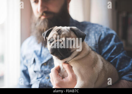 Giovane uomo barbuto che trasportano il cane in armi Foto Stock