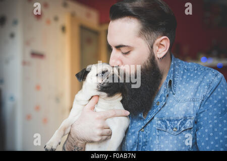 Giovane uomo barbuto baciare cane in armi Foto Stock