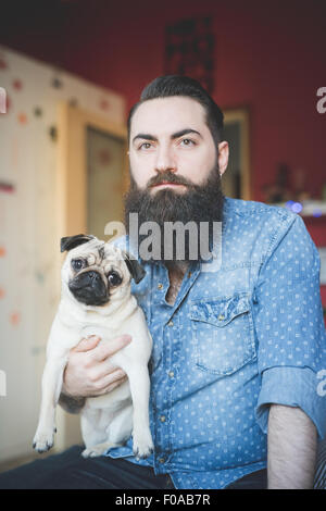 Giovane uomo barbuto che trasportano il cane in armi Foto Stock