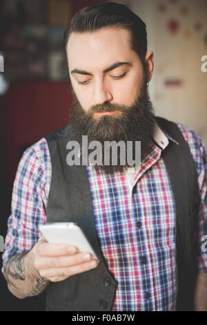 Giovane uomo barbuto utilizza lo smartphone in camera Foto Stock