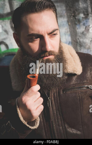 Giovane uomo barbuto tubo di fumo dal muro di graffiti Foto Stock