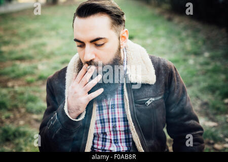 Giovane uomo barbuto di fumare in posizione di parcheggio Foto Stock