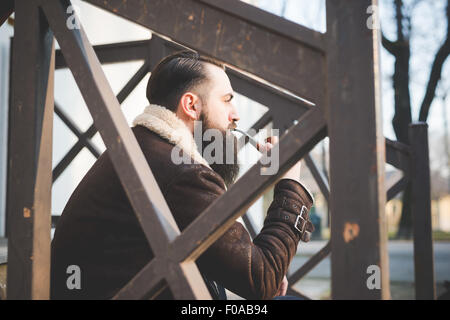 Giovane uomo barbuto tubo di fumo sui passi Foto Stock