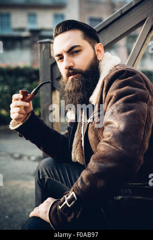 Giovane uomo barbuto tubo di fumo sui passi Foto Stock