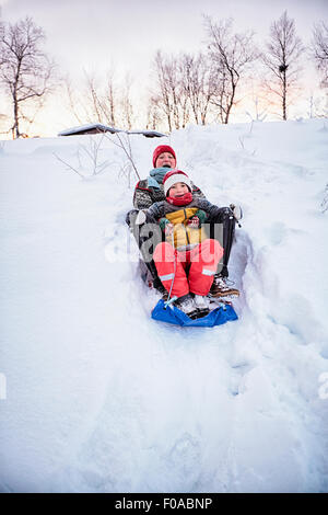 Due fratelli giocando sul toboga sulla coperta di neve hill, Hemavan,Svezia Foto Stock