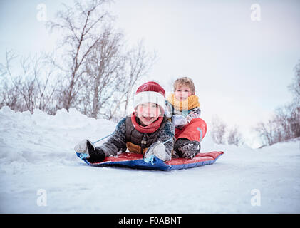 Basso angolo vista di due fratelli sul toboga sulla coperta di neve hill, Hemavan,Svezia Foto Stock