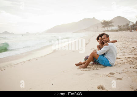 Giovane seduto sulla spiaggia, Rio de Janeiro, Brasile Foto Stock