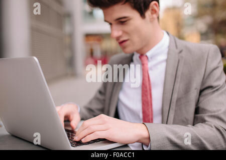 Città giovane imprenditore digitando su computer portatile presso cafè sul marciapiede Foto Stock