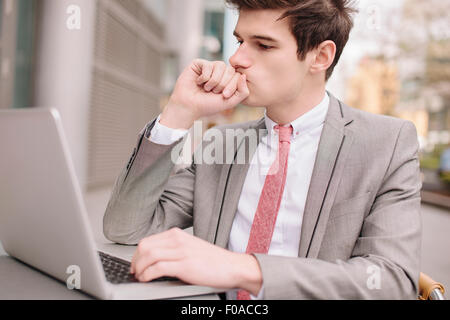 Preoccupato per il giovane imprenditore città utilizzando computer portatile presso cafè sul marciapiede Foto Stock