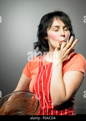 Studio shot della giovane donna con gli occhi chiusi leccare il cioccolato da dita Foto Stock