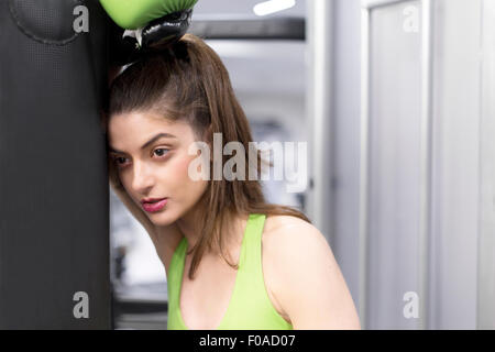 Ritratto di una giovane donna alla palestra appoggiata contro punchbag indossando guanti di inscatolamento Foto Stock