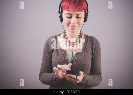 Studio Ritratto di giovane donna con corti capelli rosa scegliendo la musica sullo smartphone Foto Stock