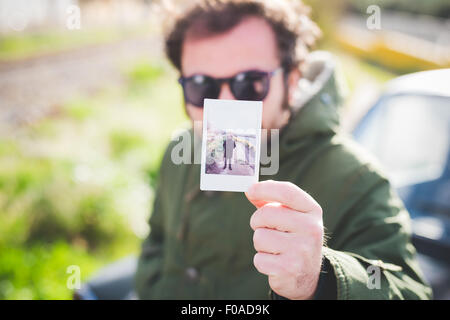 Ritratto di metà uomo adulto tenendo in mano una fotografia istantanea di se stesso Foto Stock