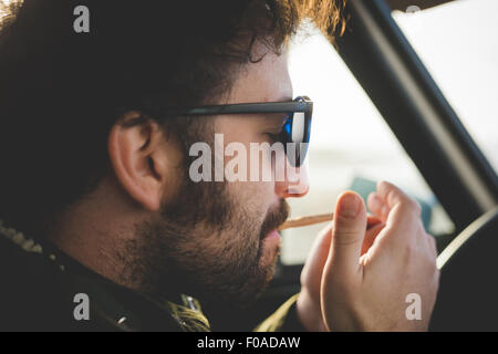 In prossimità di metà uomo adulto in auto accendere una sigaretta Foto Stock