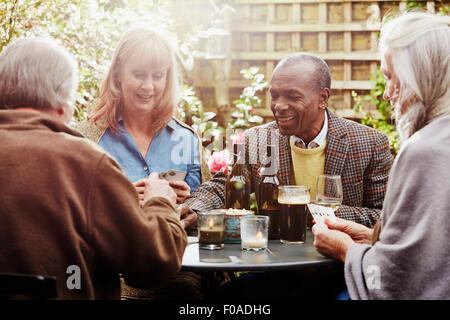 Senior gli amici a bere e giocare a carte in giardino Foto Stock