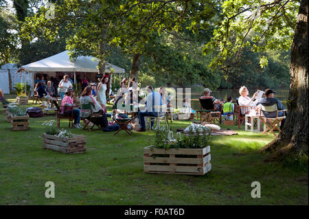 I frequentatori del festival seduti a rilassarvi e bere in ombra dalla sponda del Tagliamento a Porto Eliot Festival Cornovaglia Foto Stock