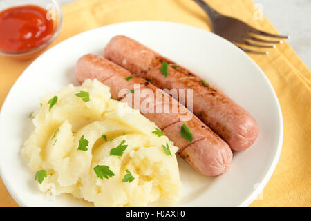 Purea di patate e salsicce con il prezzemolo e il ketchup sulla piastra bianca Foto Stock