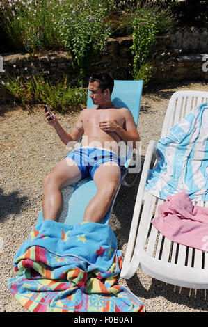 Giovane uomo di relax al sole ascoltando la musica sul suo iPhone di Apple in vacanza a gite in Francia Foto Stock