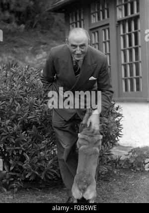 Un elegantemente vestito uomo senior giocando con il suo cane in giardino Foto Stock