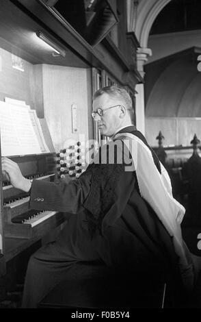 Un elegantemente vestito uomo in vesti giocando l organo in una cappella. Foto Stock