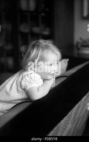 Un bambino con capelli biondi guardando sopra la schiena di un divano Foto Stock