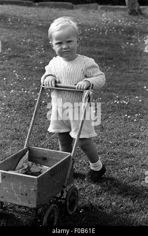 Little Boy spinta lungo un giocattolo carrello realizzato da una vecchia cassa e ruote della PRAM Foto Stock