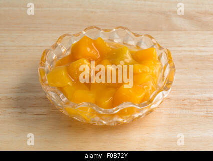Una piccola ciotola di dadini di pesche in sciroppo pesante su una tavola di legno top illuminato con luce naturale. Foto Stock