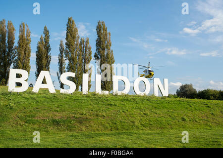 L'ora iconico segno di Basildon all'ingresso della città di Essex con la Herts ed Essex Air Ambulance sbarco accanto ad essa. Foto Stock