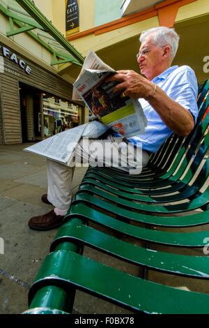 Maschio leggendo un giornale seduto su una panchina di shopping centre Salisbury Wiltshire Foto Stock