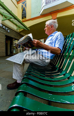 Maschio leggendo un giornale seduto su una panchina di shopping centre Salisbury Wiltshire Foto Stock