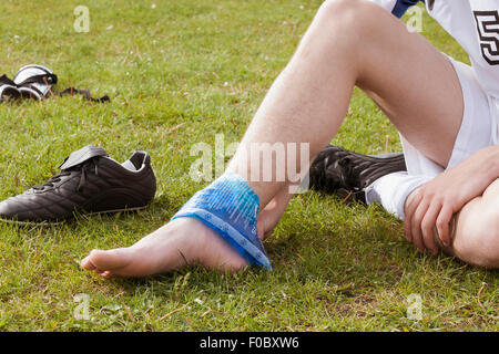 Sezione bassa del giocatore di calcio l'applicazione di ghiaccio sulla caviglia nel campo Foto Stock