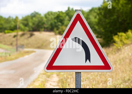 Traffico triangolare segno che indica la strada è girando a sinistra per una strada rurale sullo sfondo Foto Stock