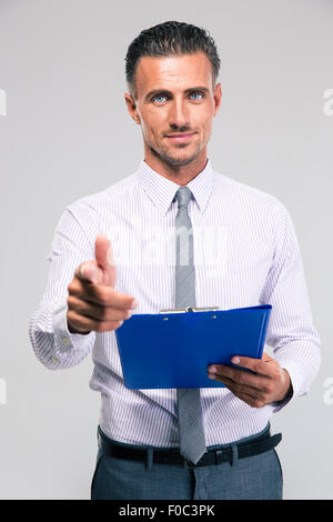 Happy businessman holding negli appunti e mostra il gesto della pistola con le dita isolato su uno sfondo bianco. Guardando la fotocamera Foto Stock