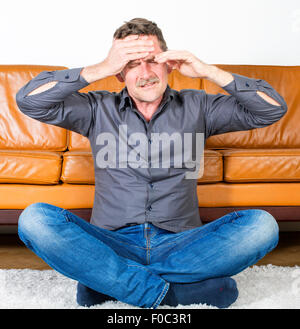 Uomo si siede sul pavimento in soggiorno con un mal di testa Foto Stock