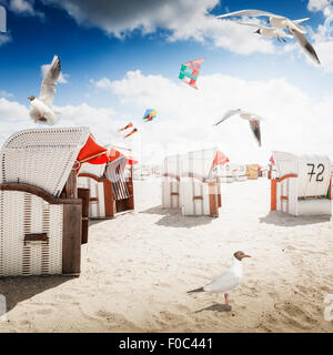 Incappucciati sedie a sdraio sulla spiaggia di sabbia. Gabbiani e volare aquiloni in blu cielo nuvoloso. Sfondo di vacanza. Costa del Mare del Nord, destina di viaggio Foto Stock