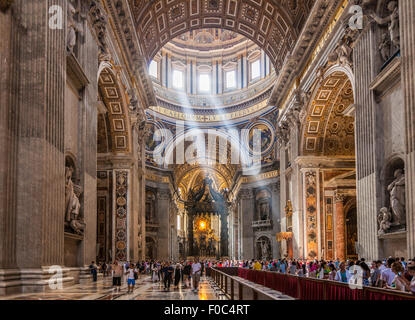 I turisti ed i visitatori all'interno della Basilica di San Pietro con alberi di luce proveniente attraverso i tetti a cupola interno Roma Italia Europa UE Foto Stock