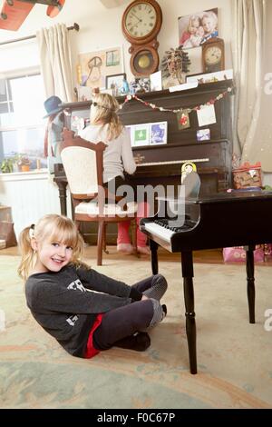 Madre seduta al pianoforte, mentre le figlie giocare in camera Foto Stock