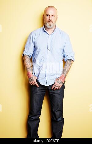 Uomo maturo con tatuaggi sulle braccia e collo, sfondo giallo Foto Stock
