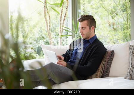 L'uomo rilassante sul divano con i piedi fino alla ricerca a tavoletta digitale Foto Stock