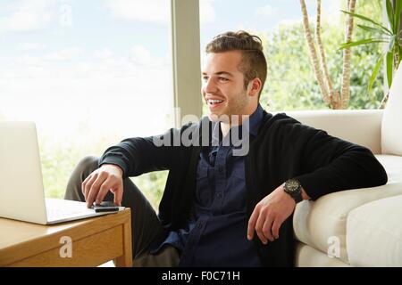 Ritratto di uomo sorridente seduto sul pavimento dello smartphone di contenimento Foto Stock