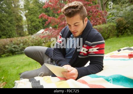 Ritratto di uomo che stabilisce nel giardino la lettura digitale compressa Foto Stock