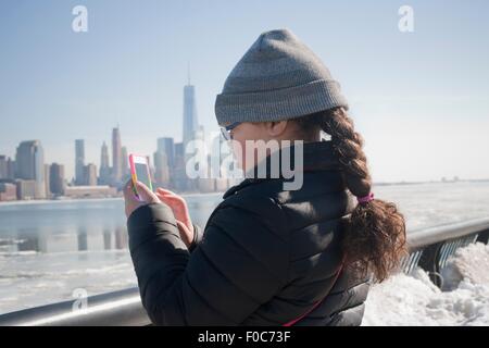 Giovane ragazza tenendo fotografia di skyline utilizza lo smartphone, New York, NY, STATI UNITI D'AMERICA Foto Stock
